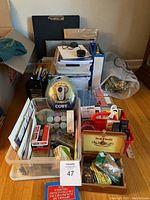 Overview of assorted office supplies in a clear plastic bin including portable radio, binders, pen holder, paper, and various packing materials.