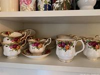 Full view of tea cups, saucers, and mugs on a shelf showing floral patterns and gold trim.