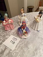 Lot of four Royal Doulton Bo-Peep porcelain figurines displayed on a lace tablecloth.