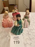 Four Royal Doulton porcelain figurines arranged on table, including a girl in green dress holding a bird and others in various gowns.