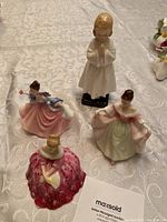Four Royal Doulton figurines displayed on fabric background, showing size and detail of dresses and poses.
