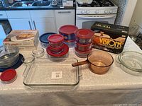 Full view of items on table including glass dishes, storage containers with red lids, baking dish, and Visions saucepan.