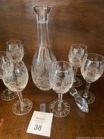 Full view of decanter with stopper and six matching wine glasses placed on wooden surface.