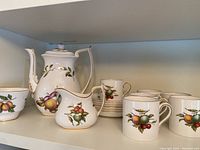 Full tea set showing teapot, creamer, cups, and saucers with colorful fruit design