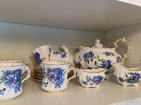 Photo showing the front view of the entire tea set including cups, saucers, teapot, creamer, and sugar bowl with blue floral pattern and gold accents.