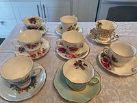 Seven bone china teacups and matching saucers arranged on a table next to each other, showing diverse floral patterns and shapes.