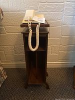 Front view of vintage telephone stand holding rotary dial phone, showing the coiled cord hanging down and storage compartments below.