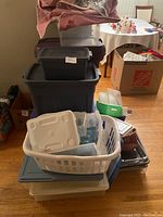 Photo showing stacked large gray, clear, and dark gray storage totes with white laundry basket and smaller containers placed on top and in front.