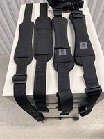 Four black clip-on luggage handles laid out on a white surface; showing padded grips and adjustable straps