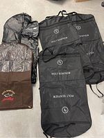 Photo showing five garment bags: three black Holt Renfrew, one brown Paul & Shark with clear window, one black Creeds.