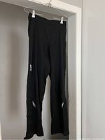 Full front view of black GORE cycling pants hanging on hanger showing straight legs with reflective marks on thighs and velcro closures at foot openings.