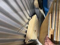 Stack of natural pine shelving boards with metal shelf pins attached, positioned inside a storage unit.