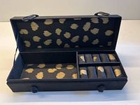 Black rectangular jewelry organizer with black and gold spotted fabric interior. Organizer has multiple compartments and padded ring holders.