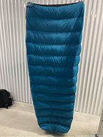 Blue tapered sleeping bag hanging showing full length and foot end, horizontal baffle stitching visible.