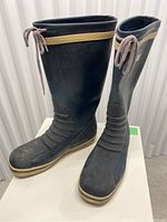 Two black rubber Gill rain boots shown from front and side, with brown-beige drawstring at top edges, beige stripe near the top, front textured panels, and rugged sole.