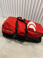 Front side view of red and black Salomon rolling duffle bag with white logo and carrying straps handles on top.