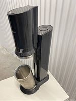 Full soda maker machine with glass bottle inserted at base, showing compact design and metal base of bottle