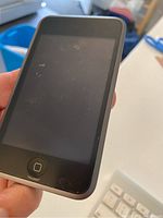 Front view of Apple iPod showing black screen and home button held in hand.