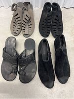 Top view of four pairs of women's shoes including taupe and black gladiator sandals, black ankle boots, and black flat sandals.