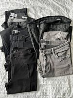 Five pairs of women's pants and jeans stacked together showing colors and styles.