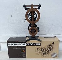 Assembled mechanical clock placed on top of the ABONG mechanical clock kit box, showing front view of clock with large and small gear dials and Roman numerals.