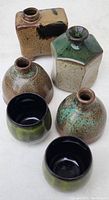 Overview photo showing three bud vases with various glazes and two black and green sake cups.