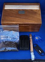 Full lot overview showing wooden humidor, cigar cutters, leather case, cigar, and humidifying material in zip-lock bag.