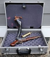 Overview of foam-lined aluminum work gear box open showing Hadley 1760 replica flintlock pistol, horn-shaped powder flask, and brass powder flask inside.