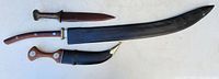 Full view of the three items: two daggers and one large curved sword with brown handle, leather sheaths.