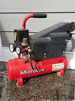 Side view of Microlux air compressor showing red tank, black top housing, red handle, and pressure gauges.
