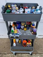 Full view of three-tier metal cart with a top tier filled with multiple small jars and bottles of modeling paint.