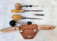 Wide view of entire tool lot showing various wooden handled tools including the Flexcut draw cutter, scratch awls, drill bits, and leather sheath.