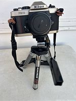 Nikon FM10 film camera mounted on Rokunar tripod, showing front view and strap details.