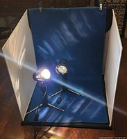 Full view of the studio with two tripod-mounted lights turned on and blue side of backdrop visible against white side panels holding light diffusion fabric.