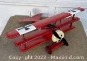 Red RC Fokker DR-1 model airplane displayed on a concrete surface, showing side profile with propeller and triplane wing structure.