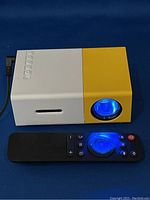 Front view of lit mini LED projector showing blue light from lens with remote control in front