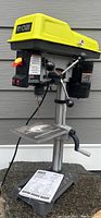 Full view of tabletop drill press on base, showing column, work table, head, power cord and manual on table.