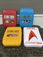Four Star Trek DVD collection cases: three plastic cases for The Original Series seasons 1-3, color-coded yellow, blue, and red; plus a white metal tin for The Animated Series.