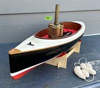 Side angled view showing black, white, and red paint with wooden stand and crochet bumpers beside the steam boat model.