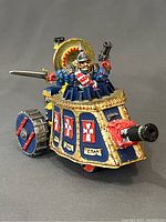 Front angled view of the Warhammer Empire Steam Tank showing painted blue and gold panels with red and white crosses and Latin inscriptions, warrior emerging from the turret with sword and pistol.