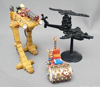 Photo showing three miniatures: yellow Scout Sentinel with rider, black Dark Eldar Cruiser on stand, and metallic spiked steam roller
