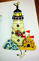 Full view of beige ceramic lighthouse clock with bird on top, wave base, sandcastle and seagull pendulum.
