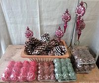 Photo showing assorted used large pine cones in a basket with six packs of small rattan balls in red, brown, and metallic green colors, plus one pack of large rattan balls in brown color.