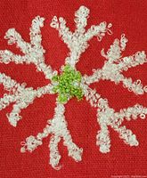 Close-up of white embroidered snowflake on red fabric showing embroidery detail and green center.