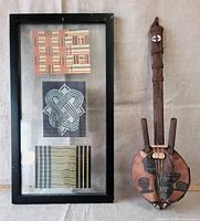 Framed textile art alongside the wooden stringed instrument, showing overall condition and relative size.