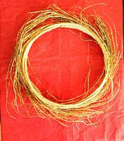 Two delicate gold-colored Christmas wreaths with twig-like texture and feathery appearance laid flat on red background.