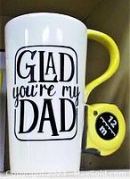 White ceramic mug with yellow tape measure handle with 'Glad You're My Dad' text in black letters.