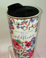 Tall ceramic coffee mug with floral design and inscription, black lid on top