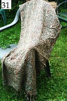 Large brown and taupe paisley patterned reversible cotton throw draped over chair outdoors on grass, showing intricate design and fringe ends.