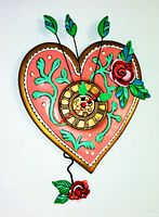 Full view of the pink heart-shaped wall clock with green leaves, red roses, and bronze clock face with Roman numerals.